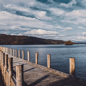 View of Windermere in the Lake District with a wooden jetty in the middle — representing the Top Tier partnership on the Partner With Us page of Sukanya The Podcast.