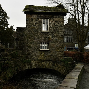 View of Bridge House in Ambleside, a 17th-century building spanning Stock Beck — representing the Ambleside Feature + Content Bundle on the Be a Guest page of Sukanya The Podcast.